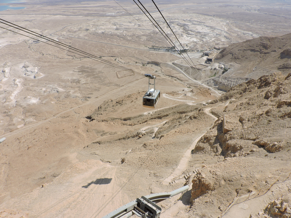 Vue aérienne d'un téléphérique descendant une colline rocheuse avec un paysage désertique.