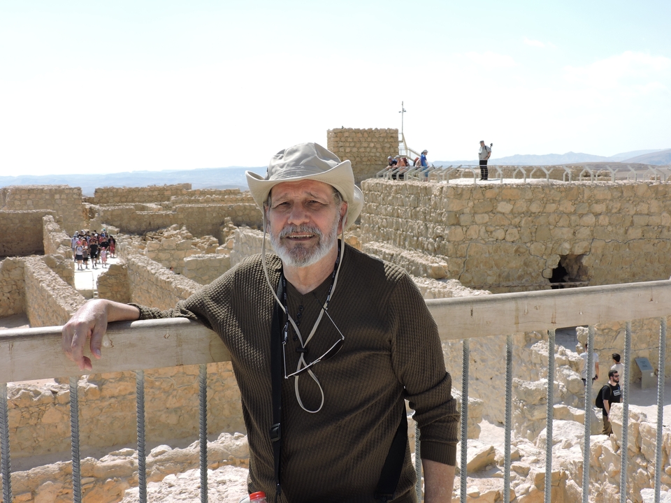 Homme souriant devant d'anciennes ruines en pierre sur fond de paysage.