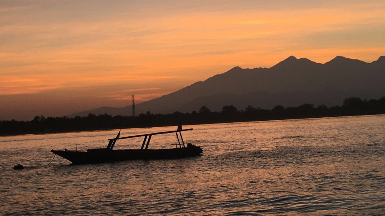 Bootssilhouette auf dem Wasser mit Bergen im Hintergrund bei Sonnenuntergang.