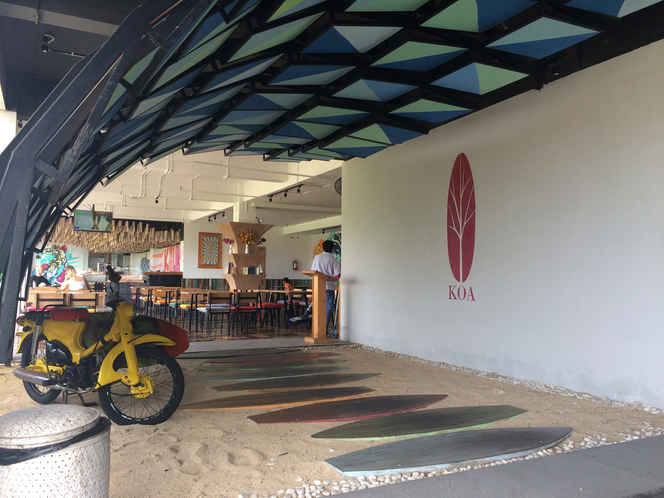 Trendy open-air café with colourful surf-inspired decor, a yellow motorbike and KOA logo on the wall.