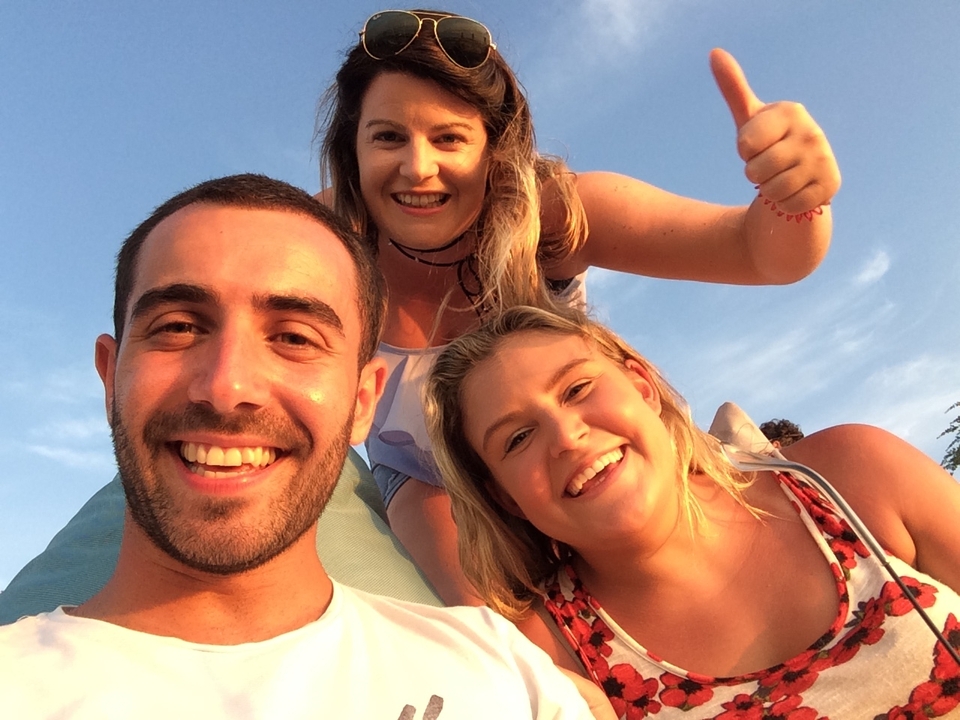 Close-up selfie of three friends smiling in warm sunset light on the beach.