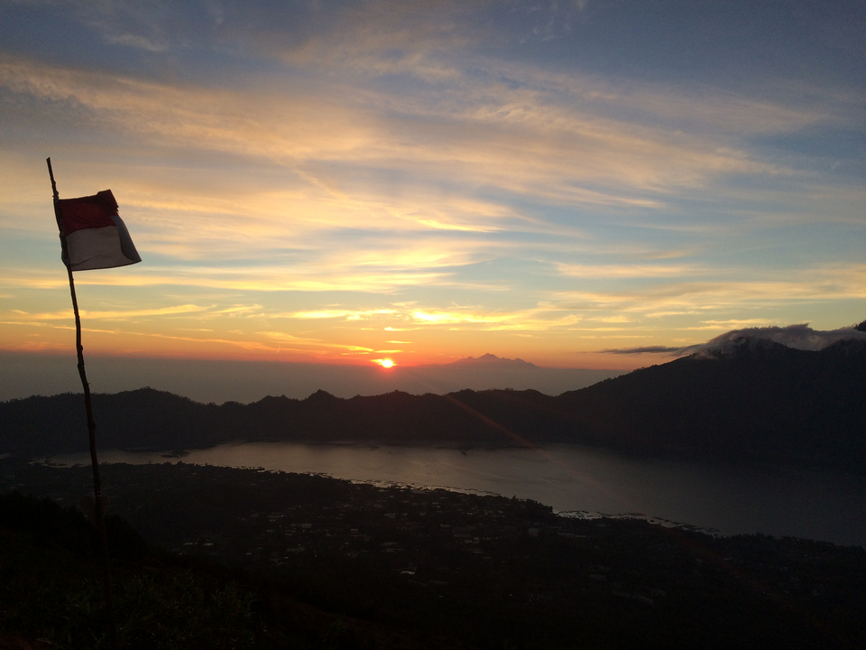 Stunning sunrise over island-dotted lake with Indonesian flag in foreground and colourful sky.