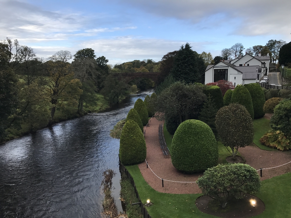 Jardin riverain avec des haies bien entretenues et un pont.