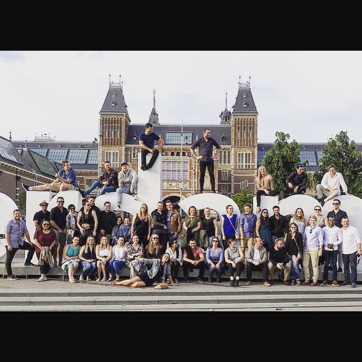 Grand groupe de personnes posant devant un panneau avec un grand bâtiment derrière.