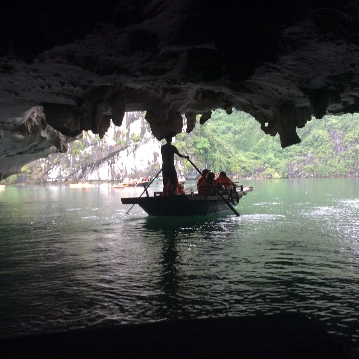 Des personnes sur un bateau se détachant sur l'ouverture d'une grotte avec des formations calcaires.