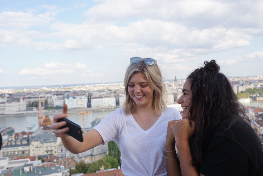 Deux femmes prenant un selfie avec une vue de la ville en arrière-plan.