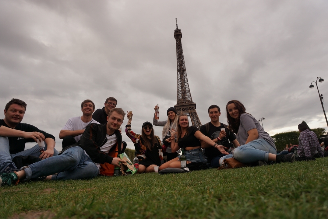 Groupe de personnes assises sur l'herbe avec la Tour Eiffel en arrière-plan.