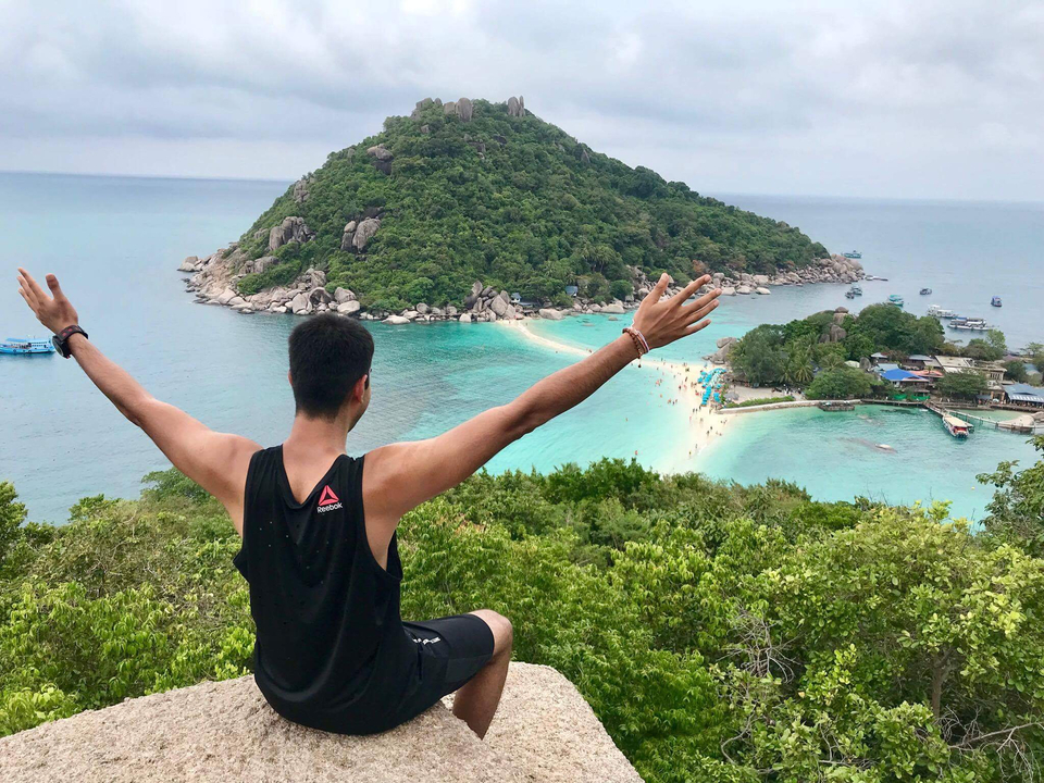 Person with arms raised overlooking a scenic beach and island.