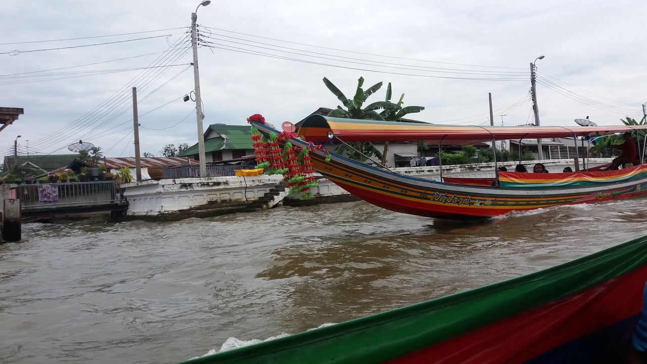 Bateau long traditionnel naviguant sur une rivière bordée de maisons.