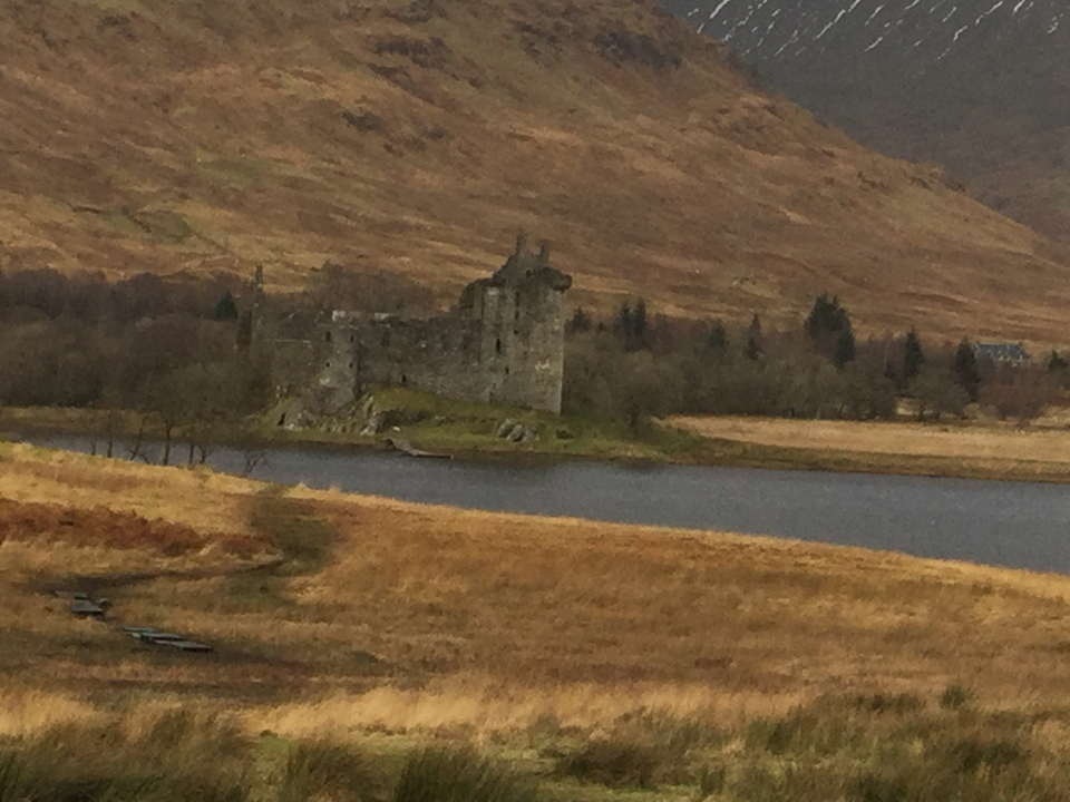 Ruines d'un château au bord d'un lac dans un paysage vallonné.