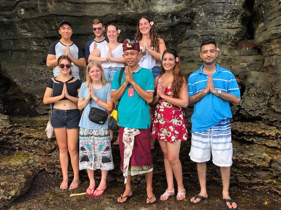 Personnes posant avec une personne locale en tenue culturelle sur un fond rocheux.