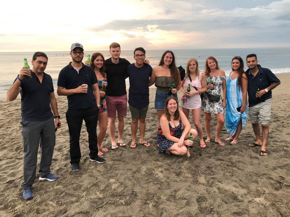 Photo de groupe sur une plage en train de boire un verre avec l'océan en arrière-plan.