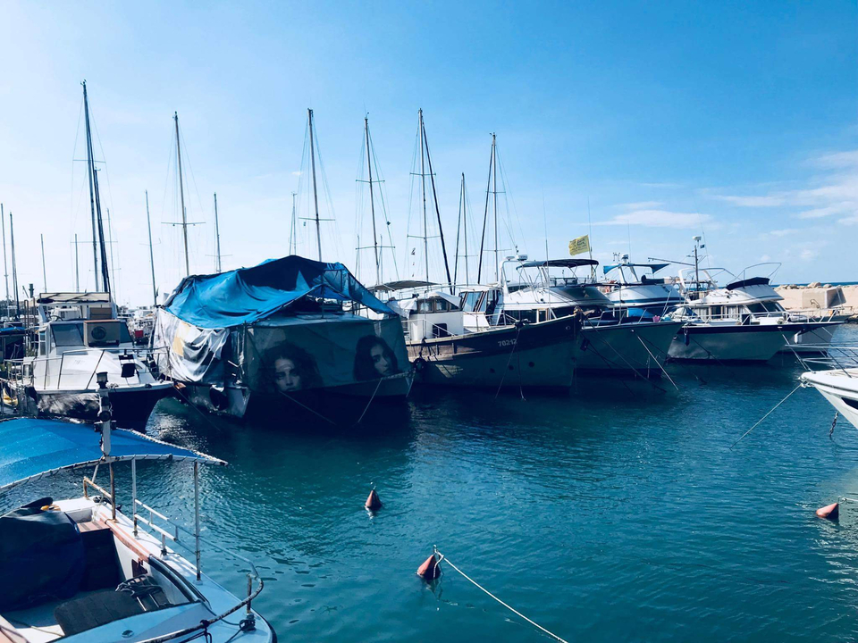 Row of sailboats covered with tarps in a turquoise harbor.
