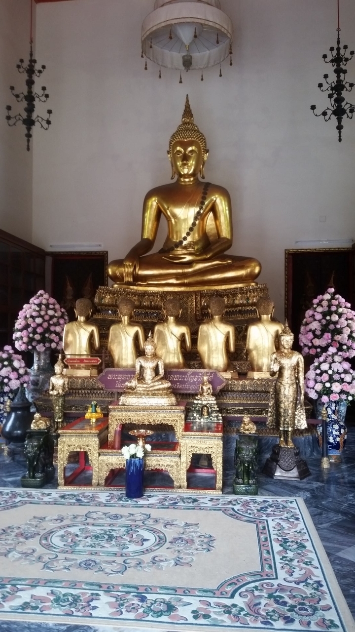Statue de Bouddha en or entourée de personnages plus petits et de fleurs.