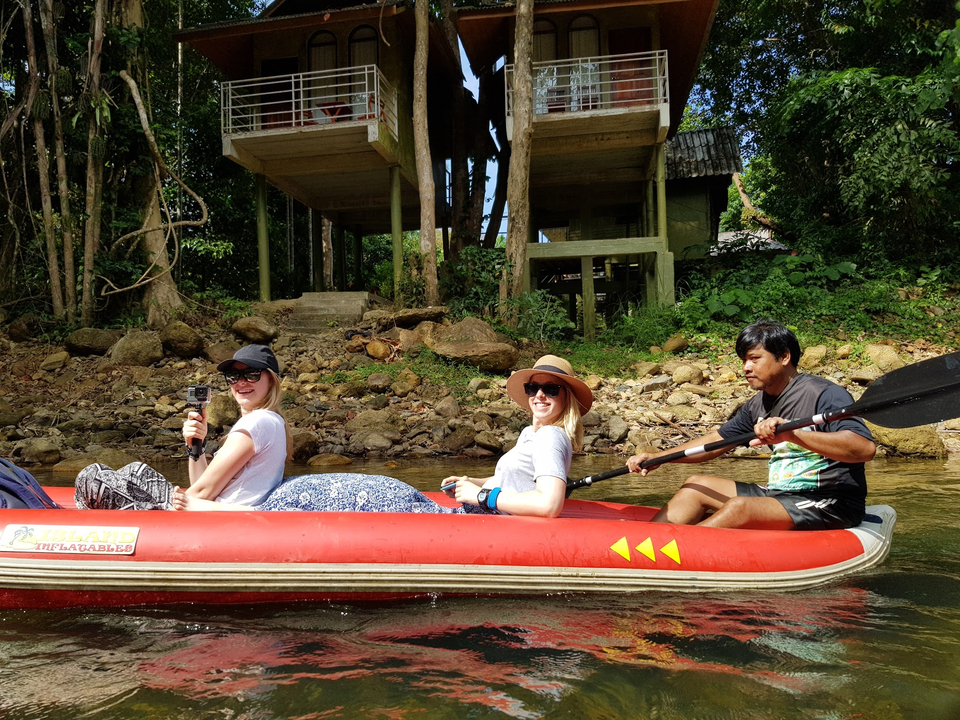 Trois personnes font du canoë sur une rivière pittoresque entourée de forêts.