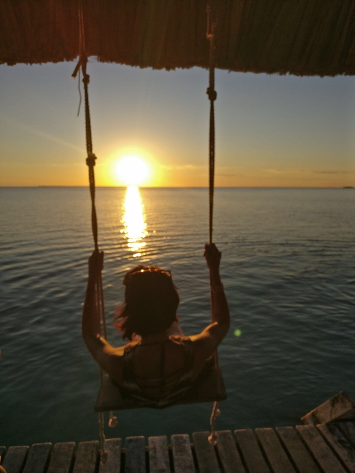 Silhouette d'une personne sur une balançoire au coucher du soleil sur l'eau.