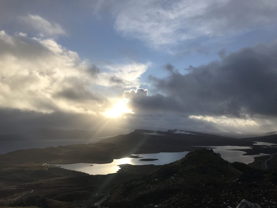 Dramatic landscape with water, hills, and sunlight breaking through clouds.