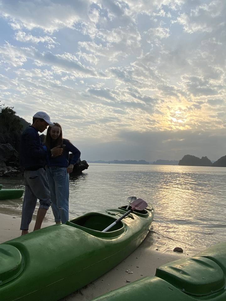 Deux personnes avec un kayak sur une plage au coucher du soleil.
