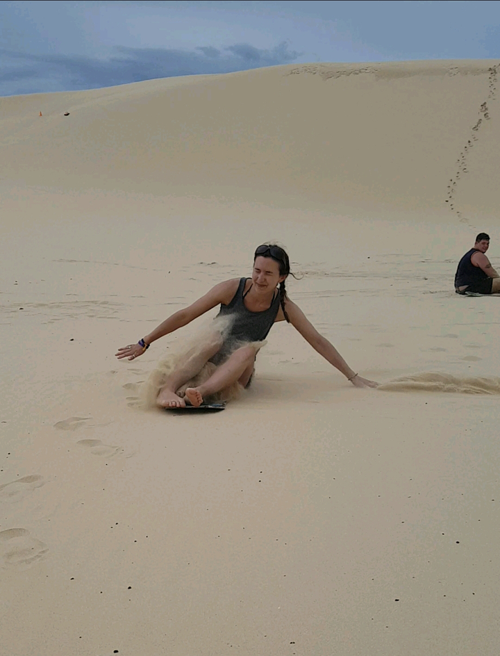 Person sliding on sand dunes, laughing.