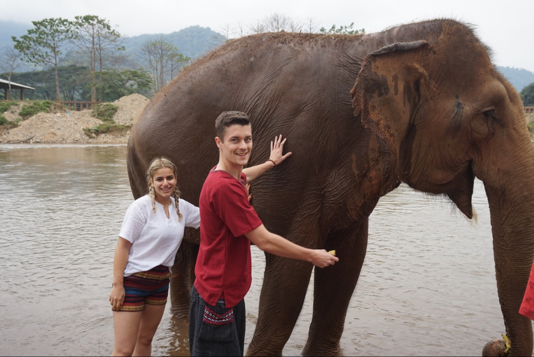 Homme et femme caressant un éléphant dans l'eau.