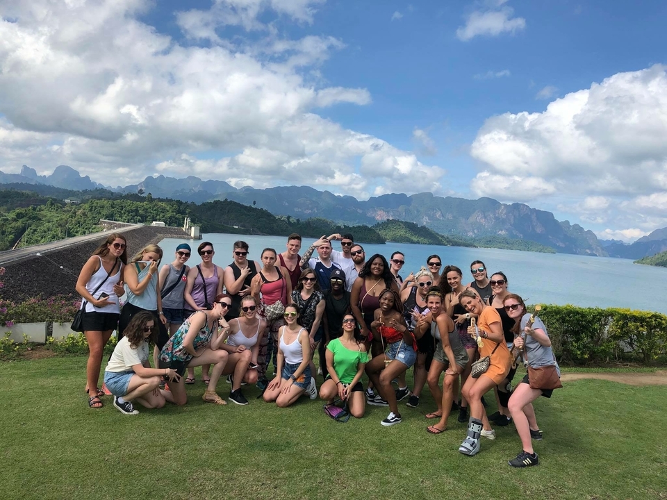 Grand groupe posant avec des montagnes et un lac en arrière-plan.