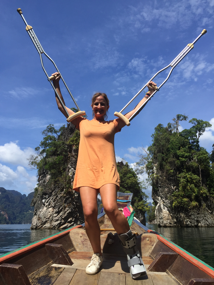 Femme souriante tenant des béquilles avec des falaises calcaires en arrière-plan.