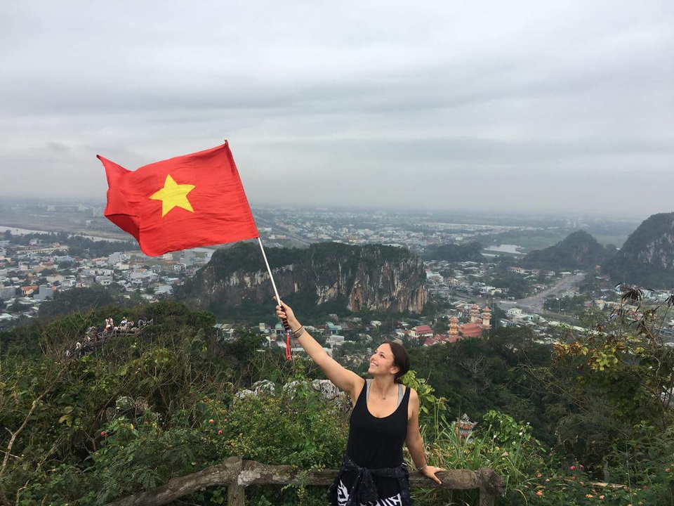 Femme tenant un drapeau vietnamien avec une vue panoramique des montagnes et de la ville.