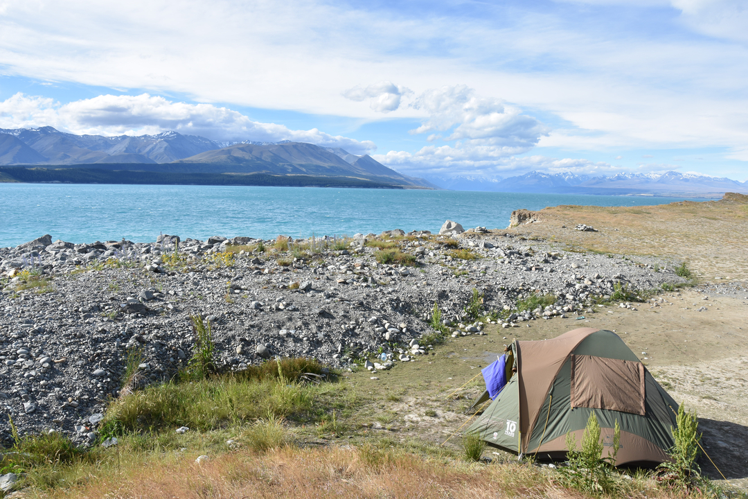 Installation d'une tente au bord d'un lac avec des montagnes en arrière-plan.
