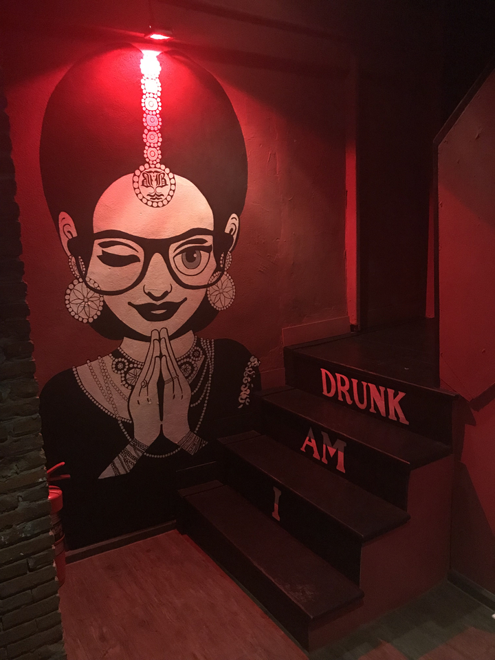 Inside a red-lit room with a painting of a winking person on the wall.