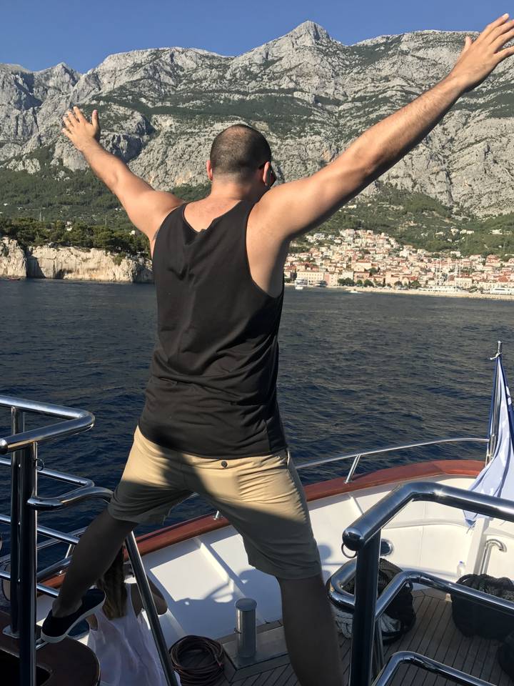 Homme posant sur un bateau avec la mer et les montagnes