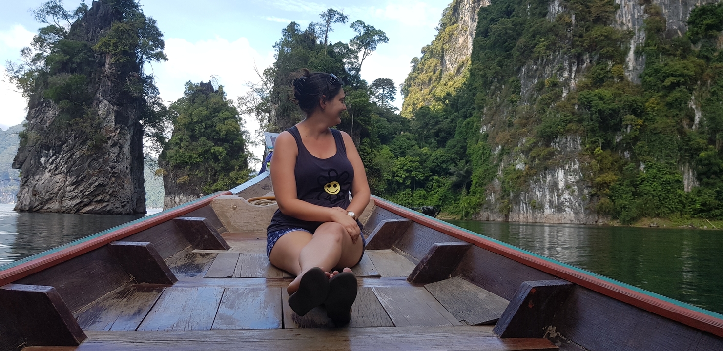 Femme assise à la proue d'un bateau entouré de falaises calcaires et d'arbres.