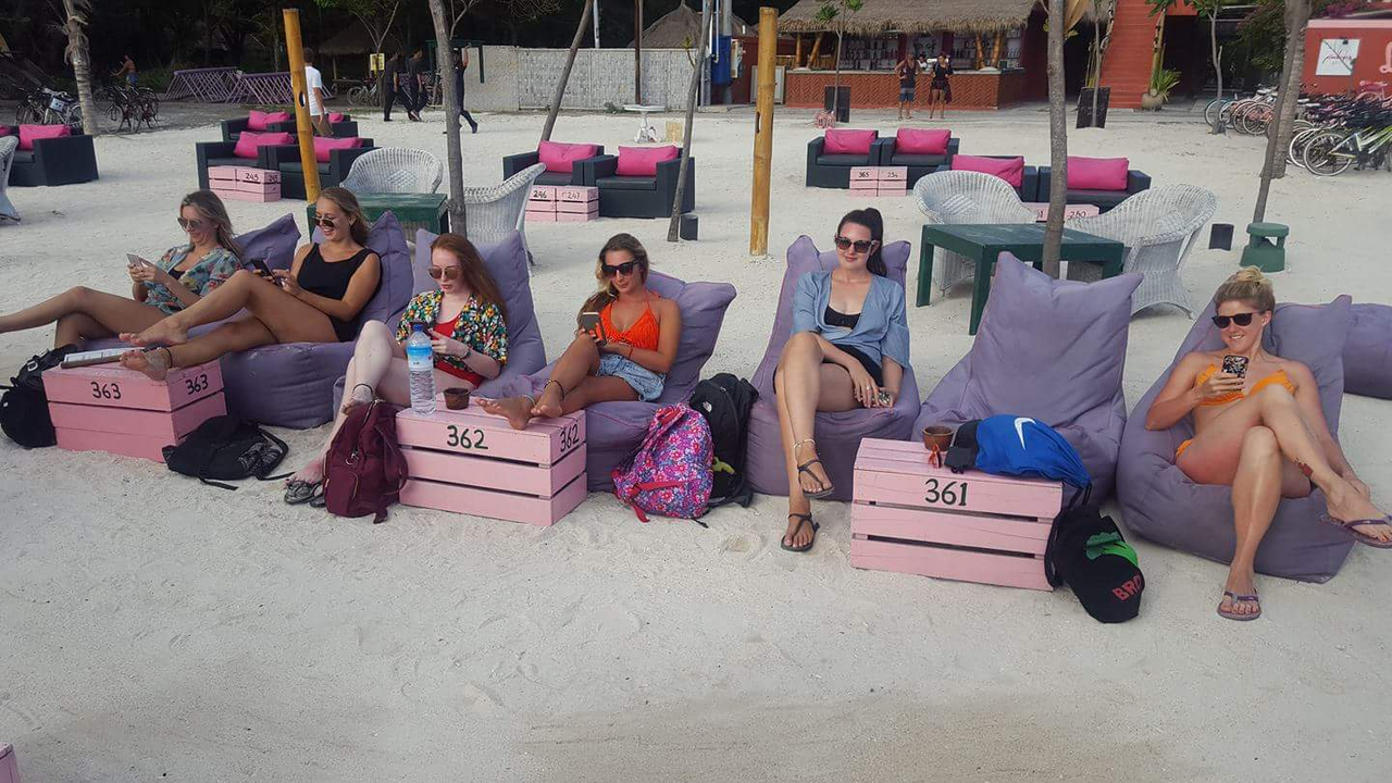 People relaxing on the beach while using their phones.