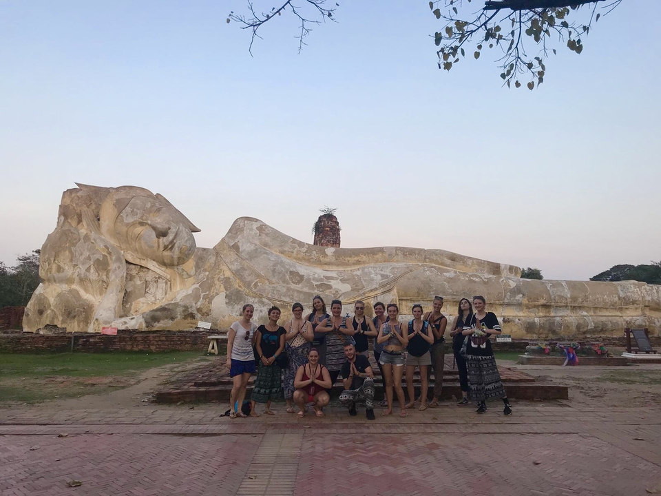 Group in front of a large reclining Buddha statue in an outdoor setting.