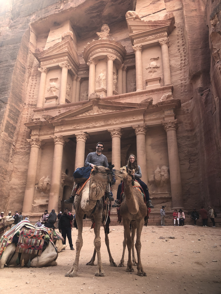 Des gens à dos de chameaux devant un bâtiment historique