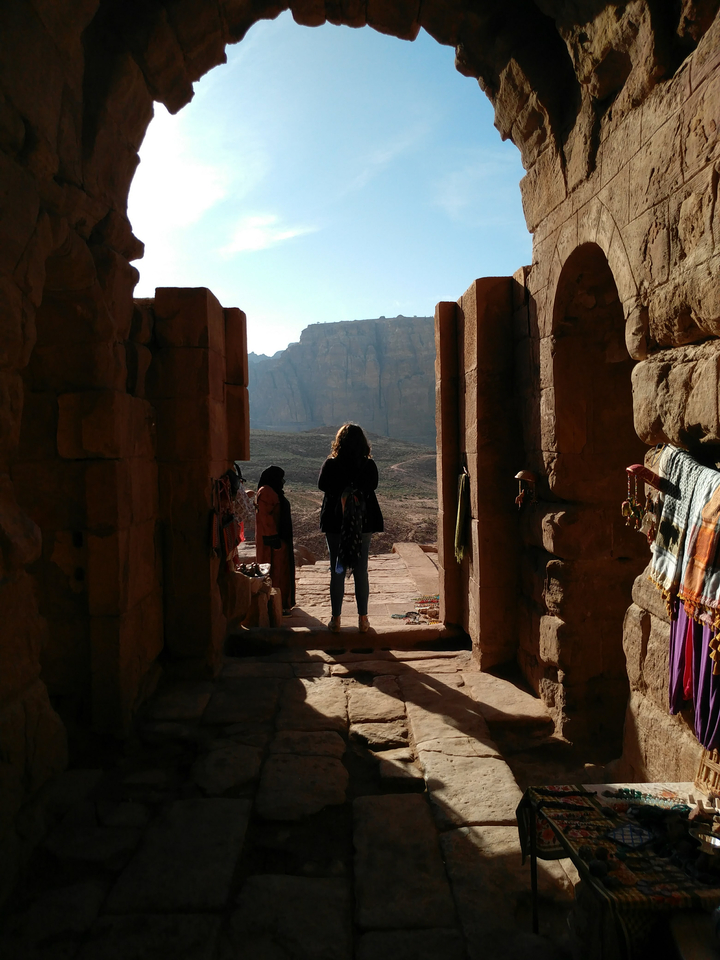 Back view of a person standing between stone pillars overlooking a canyon.