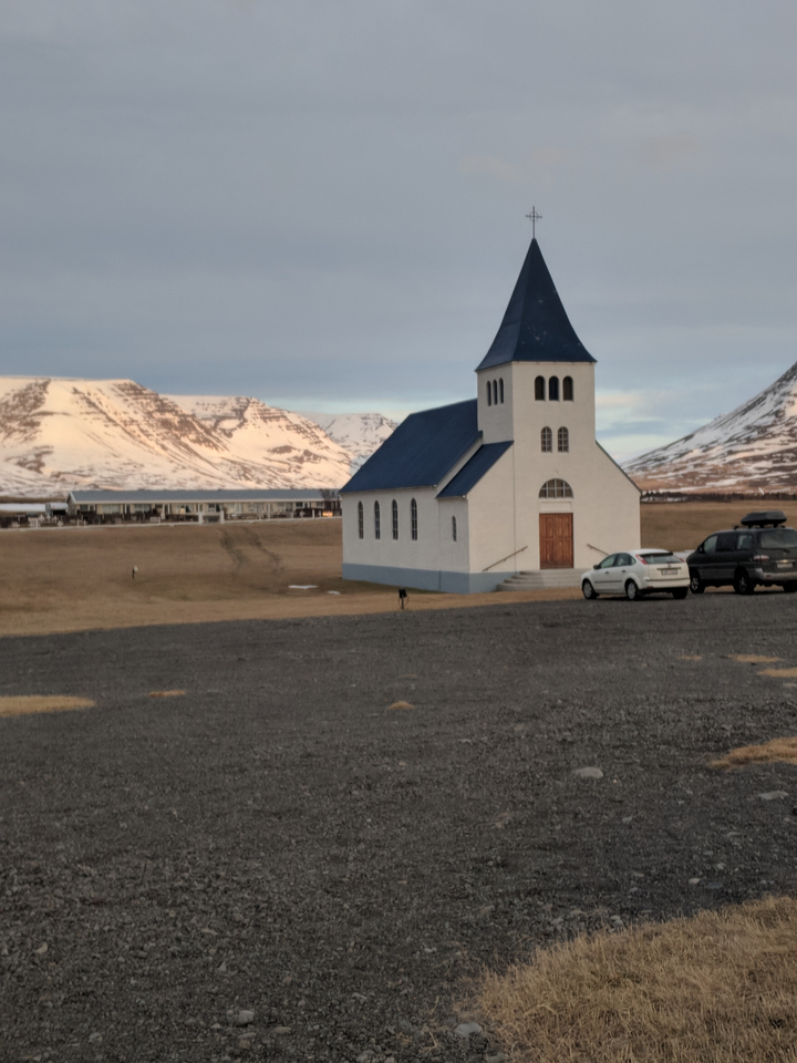 White church in a snowy landscape with parked cars.