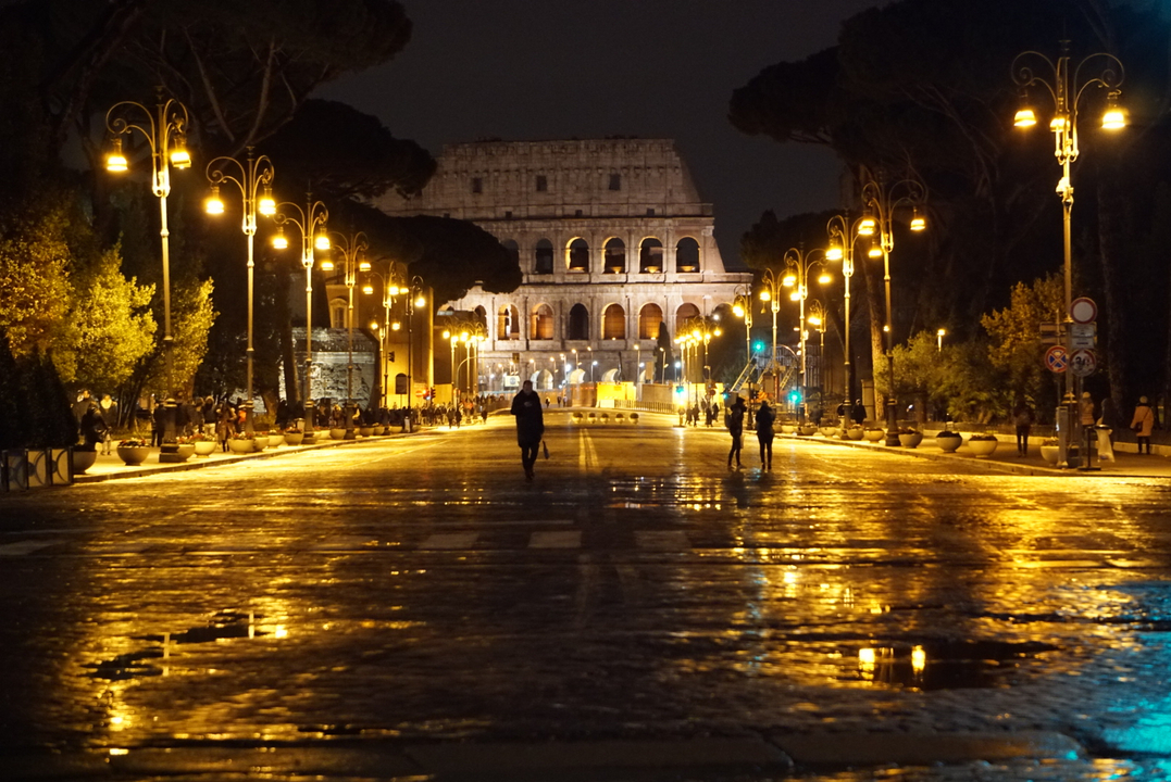 Colisée illuminé la nuit avec une route réfléchissante mouillée.