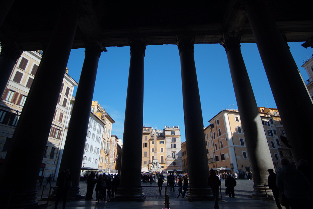Vue à travers des colonnes sur une place de ville avec des bâtiments.