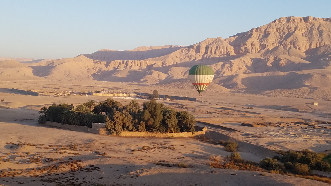 Montgolfière survolant un paysage désertique au lever du soleil.