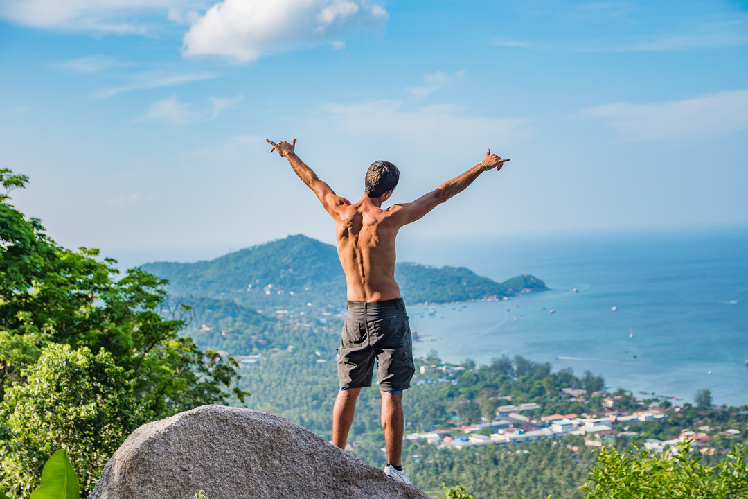Person with arms raised overlooking a coastal landscape.