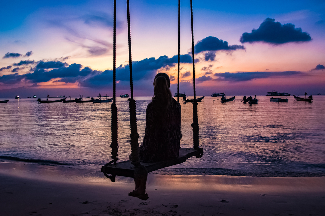 Silhouette of a person on a swing at the beach during sunset.
