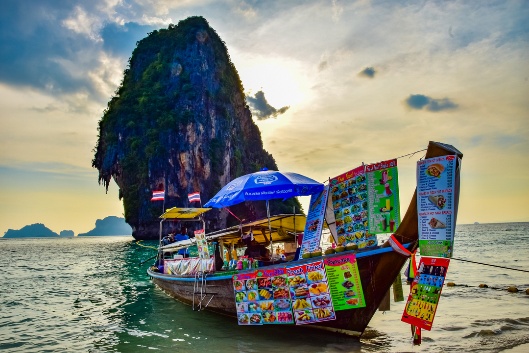 Colorful long-tail boat and karst rock formations at sea.