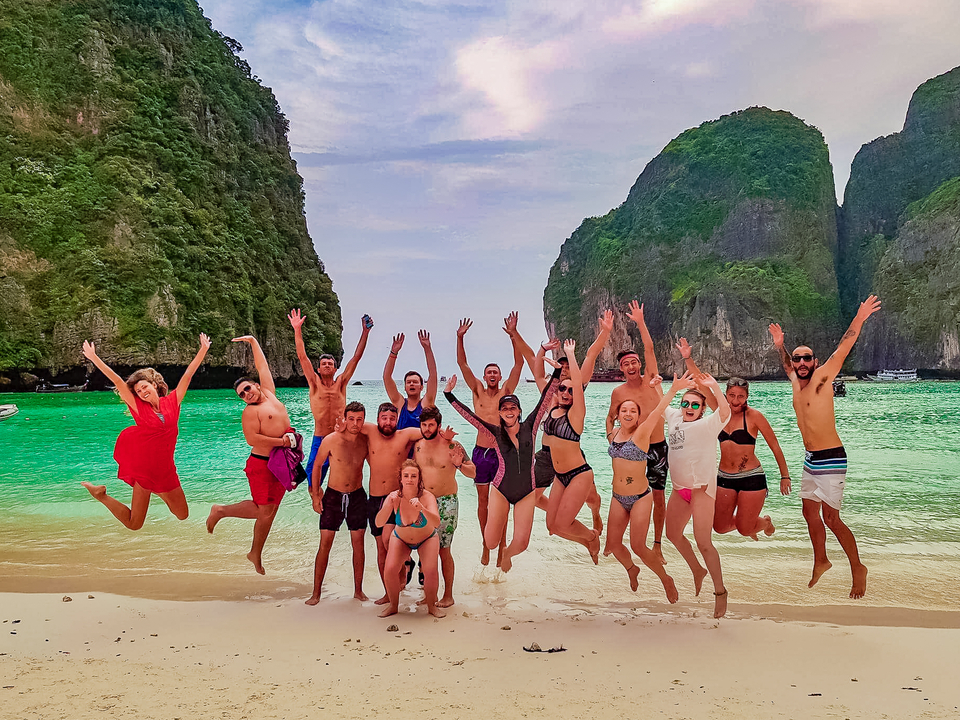 Group of people jumping on a beach surrounded by cliffs.