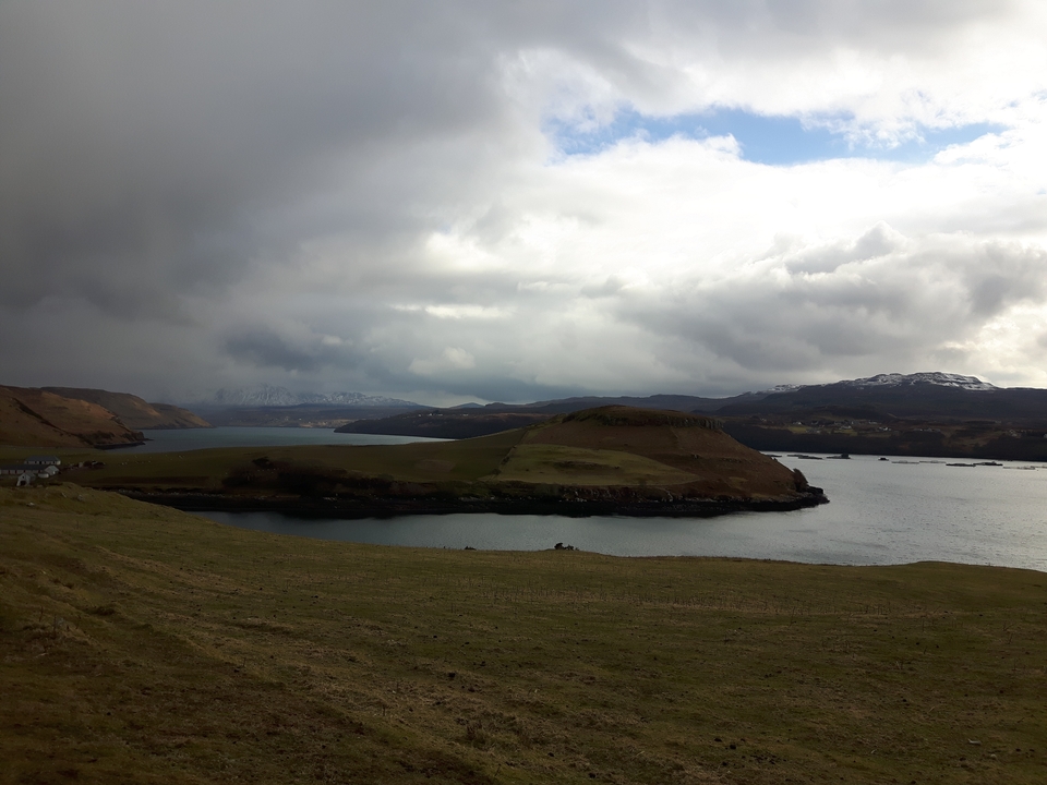 Des collines ondulantes et un ciel couvert au-dessus d'une étendue d'eau.
