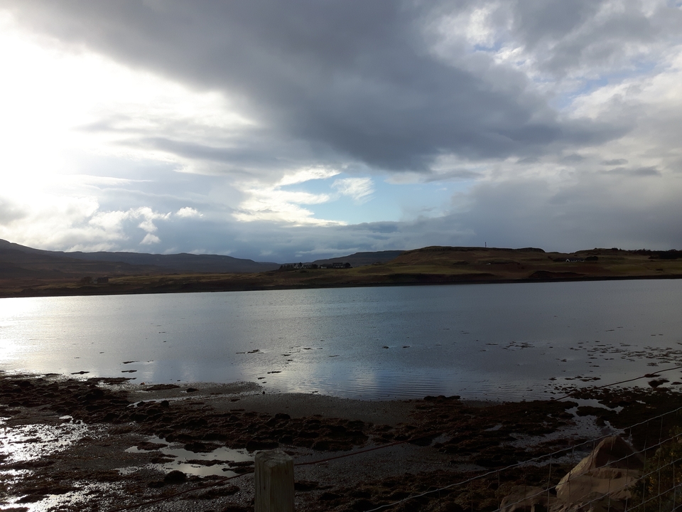 Lac calme avec des collines environnantes et un ciel partiellement nuageux.