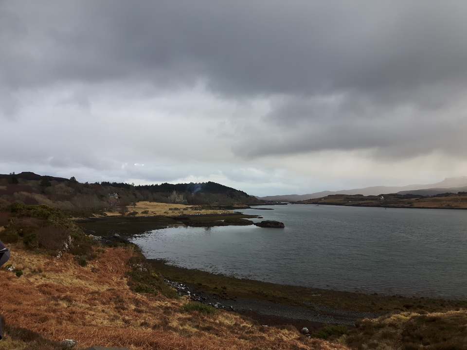 Rivière traversant un paysage vallonné sous un ciel nuageux.