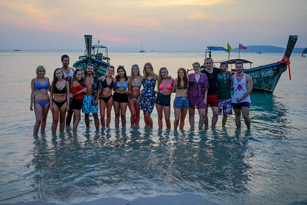 A group of people standing in water with boats in the background.