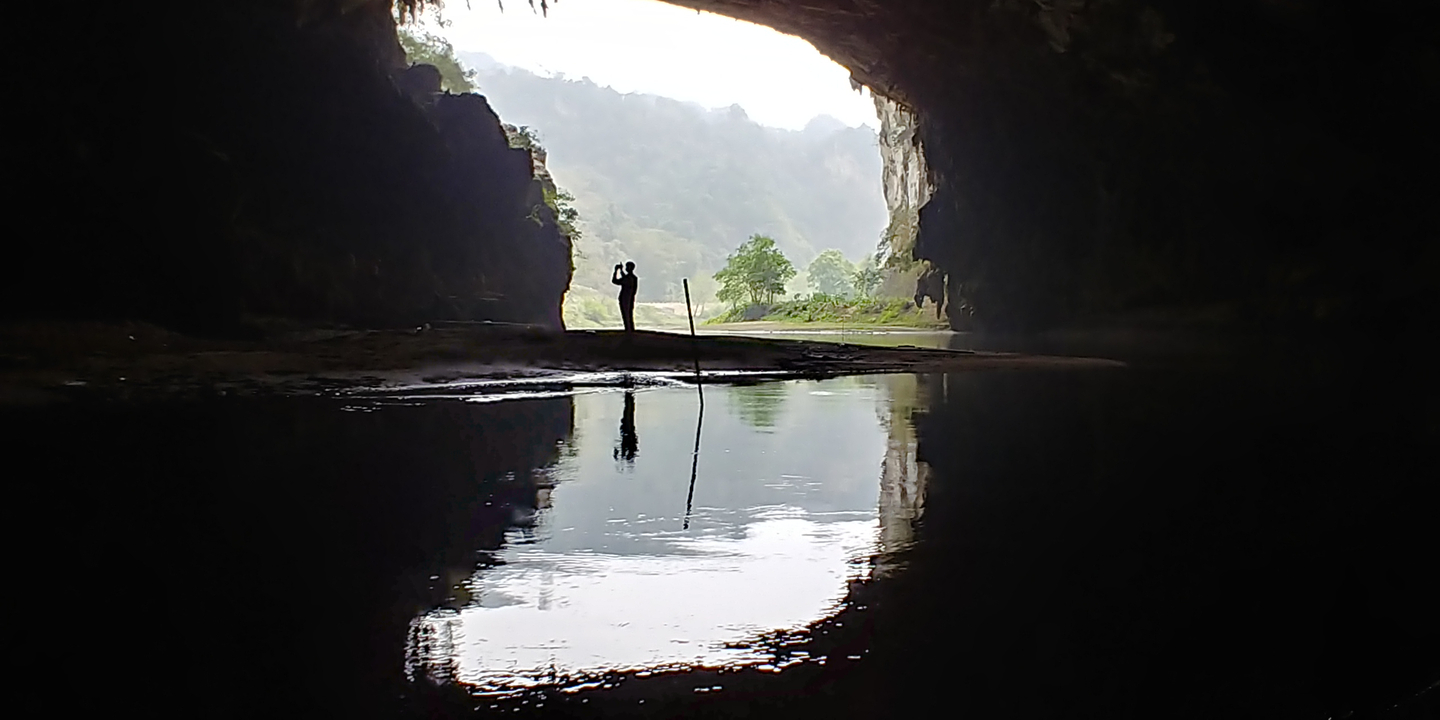 Silhouette d'une personne debout à l'entrée d'une grotte avec un reflet sur l'eau.