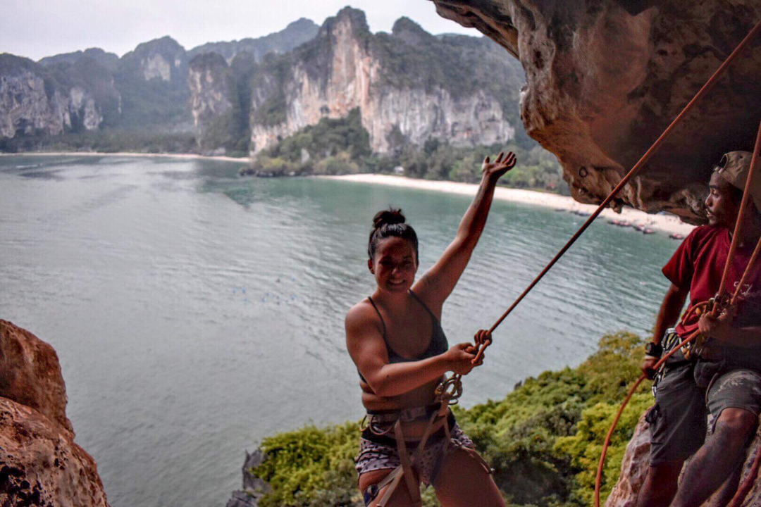 Person climbing on a rock face with an ocean view behind.