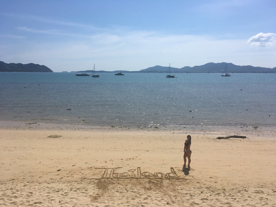 Person standing on a beach with 'Thailand' written in the sand.